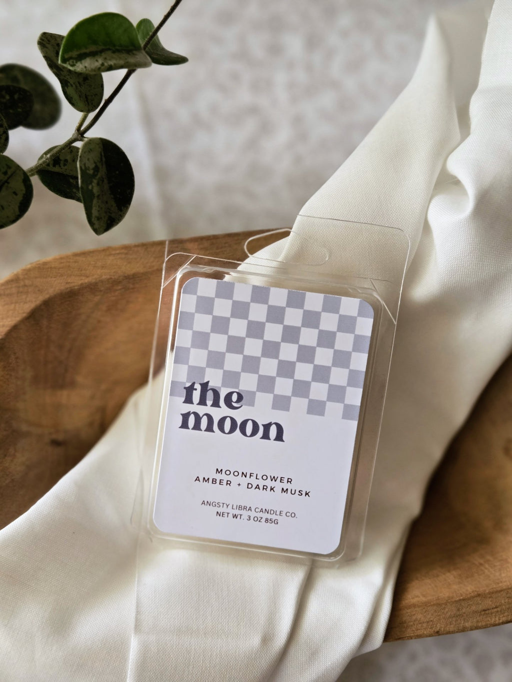 Wax melt packaging labeled 'the moon' on a white surface with a plant in the background