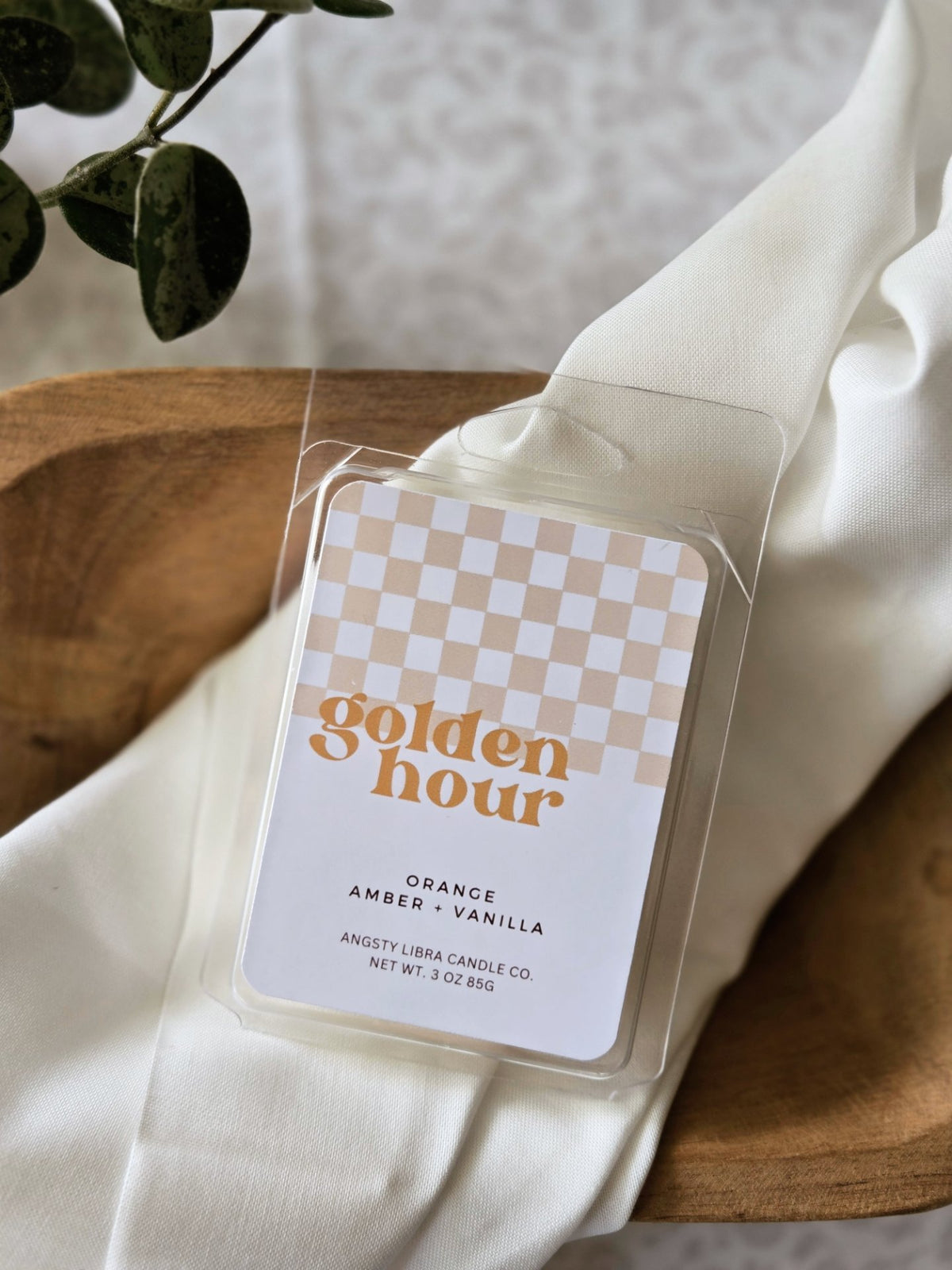Wax melt packaging labeled 'golden hour' with a checkered design on a white fabric background.