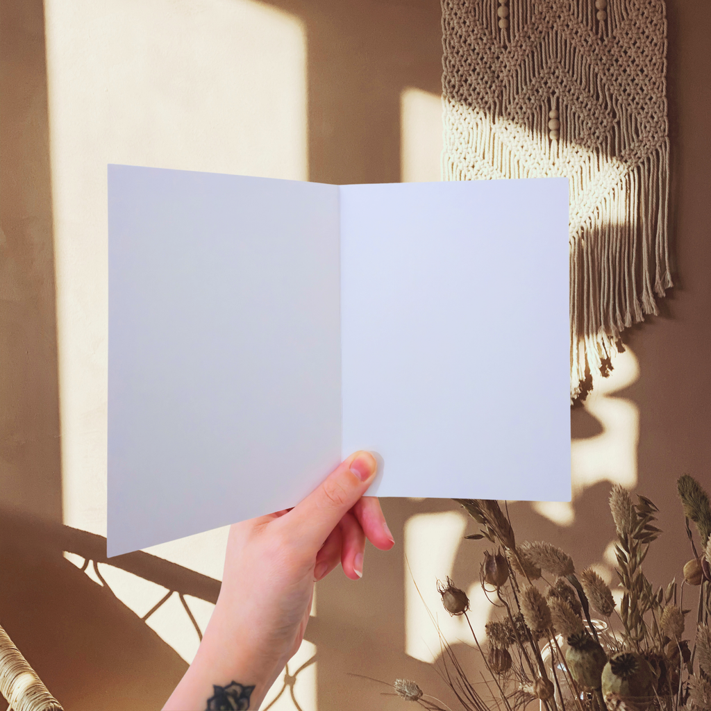 Hand holding a blank white greeting card with macrame art and plants in the background
