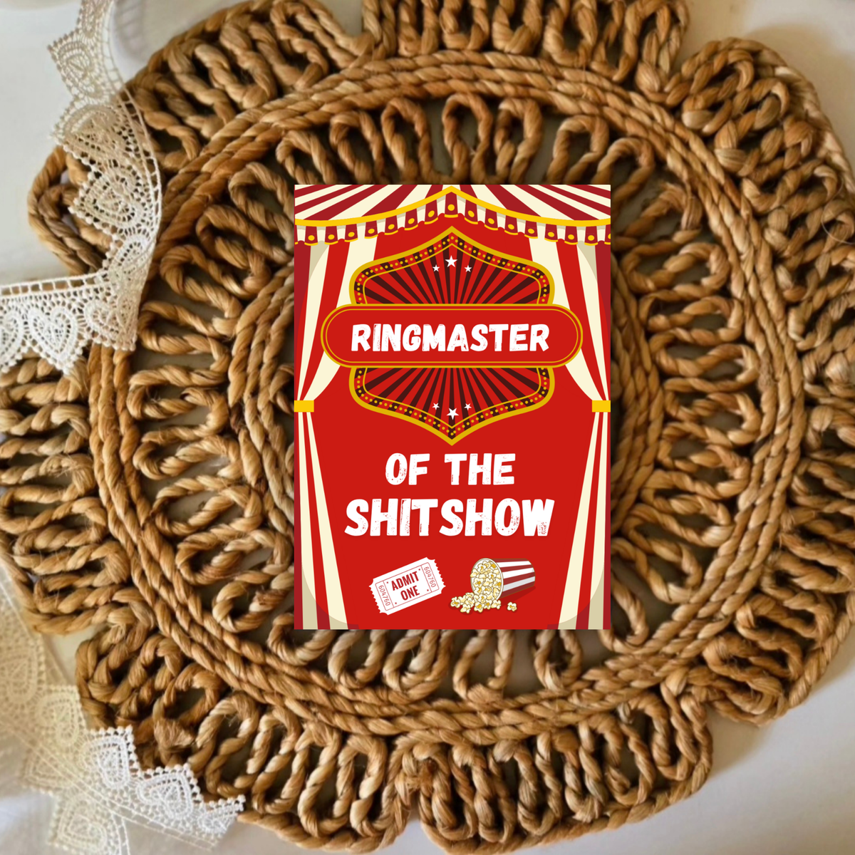 Red and white card with 'Ringmaster of the Shitshow' text on a woven mat.