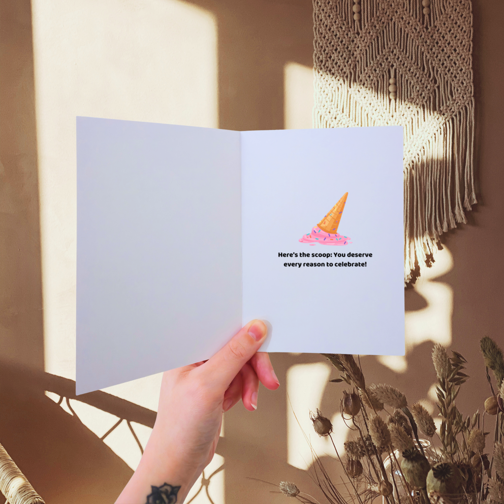 Hand holding a greeting card with a cat illustration and text, with a blurred background of plants and wall art.