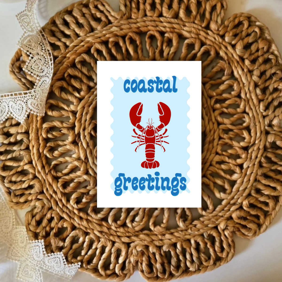 Round woven placemat with a card featuring a lobster and 'coastal greetings' text.