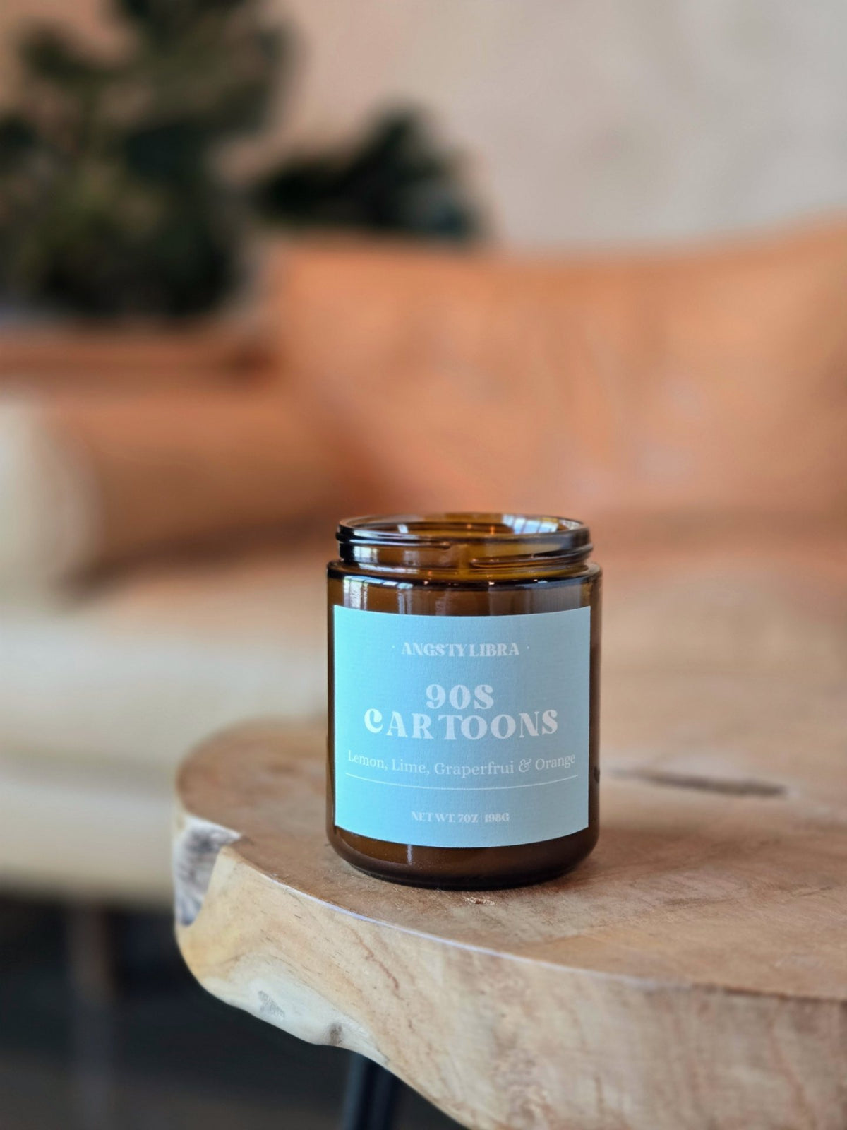 Candle in a glass jar labeled '90s Cartoons' on a wooden surface with a blurred background